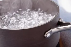 Grey stock pot with water that is at a roaring boil. Large bubbles and steam are seen in the pot.